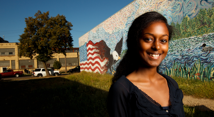 Undergraduate Justice and Peace Studies major Heaven Fekadu stands in front of a mural she helped paint in south Minneapolis. Photo by Mike Ekern '02.
