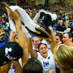 Kia Johnson hoists the national championship trophy as her teammates celebrate following the NCAA Division III Volleyball title game in Holland, Michigan Nov. 17, 2012. UST won the title after coming back from two sets down to defeat number one ranked Calvin 3-2. (Photo by Mark Brown)