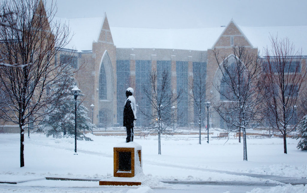 The statue of John Ireland stands amid falling snow on the lower quad April 11. (Photo by Mike Ekern '02)