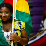 Flag bearer and student Natacha Eguida smiles while wrapped in the flag of her native Togo in Schoenecker Arena prior to the inauguration. (Photo by Mark Brown)
