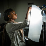A student applies a diffuser to a light during a video production class .