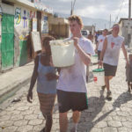 St. Thomas students Danny Burke, left, and Willie Falk, right, help Haitians - often restavecs (slave children) - carry clean water from the truck back to their homes.