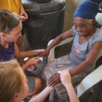 Lauren Ademite, top, and Nicole Pott, bottom, care for an elder orphan during a visit to Titanyen, the poorest rural village in Haiti. They brought her food, put lotion on her dry hands and shared prayers.