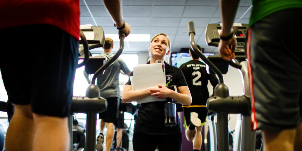Student instructor Sophie Gottsman (Exercise Science) talks with seminarians working out on elliptical machines during a Fit for Ministry class in the Anderson Athletic and Recreation complex on November 17, 2014. The course, specifically designed for seminarians from The Saint Paul Seminary School of Divinity, aims to provide physical direction for students focused on primarily intellectual studies. The class is the culmination of a collaboration between the school of divinity and the Health and Human Performance Department.