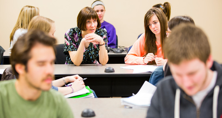 Professor Sherry Jordan (center, wearing floral dress) talks with students during a combined English and Theology course in a McNeely Hall classroom. The course is part of the Writing Across the Curriculum faculty development initiative.