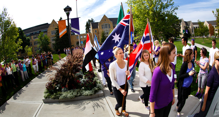 Students holding international flags walk with incoming freshmen through the lower quad amidst ranks of applauding faculty, staff and students during the freshman March Through the Arches ceremony September 3, 2013.