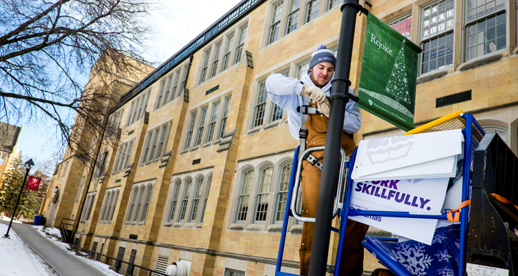 Sophomore Dan Vlourde removes a Christmas sign in order to put up a new branding sign on a lamp post outside John Roach Center for the Liberal Arts January 29, 2016.