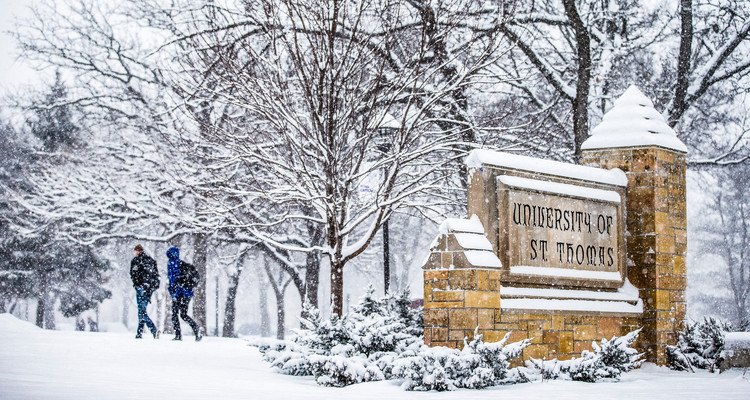 Students walk amid falling snow past the "University of St. Thomas" monumental sign at the corner of Summit and Cretin Avenues February 2, 2016.