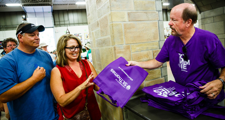 Doug Hennes, Vice President for Government Relations and Special Projects, hands out purple bags at the University of St. Thomas booth in the Education Building at the 2016 Minnesota State Fair on August 25, 2016.