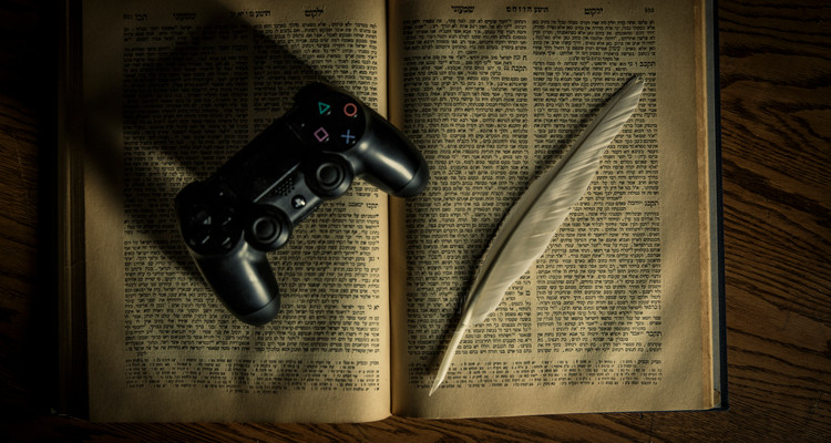 An Old Testament, a PlayStation 4 controller and a feather quill pen are shown April 12, 2017. Theology professor Corrine Carvalho and student Mike Best have done extensive work on the intersection of the Old Testament and Video Games. Taken for St. Thomas magazine.