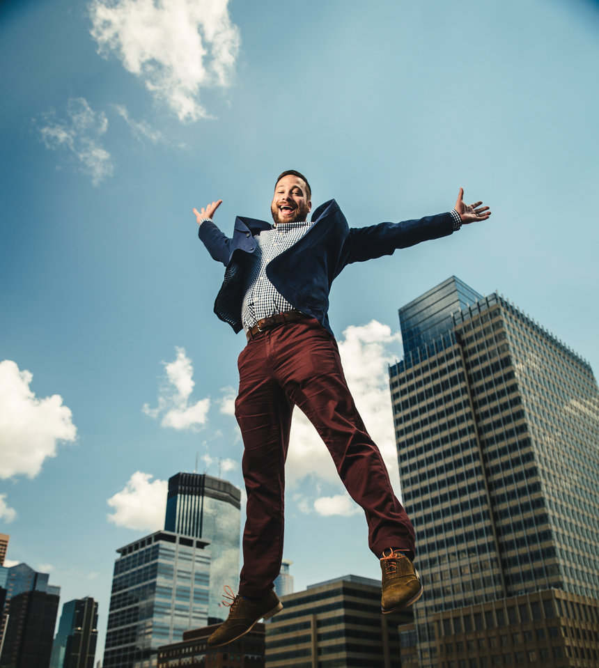Joseph Johnson earned a BA in business (04) a Law degree (07) and an MBA (08) from the University of St. Thomas. Here Johnson jumps while posing for a portrait on the roof of the School of Law building with the skyscrapers of downtown Minneapolis in the background. He was photographed on August 2, 2017 for St. Thomas Lawyer Magazine.
