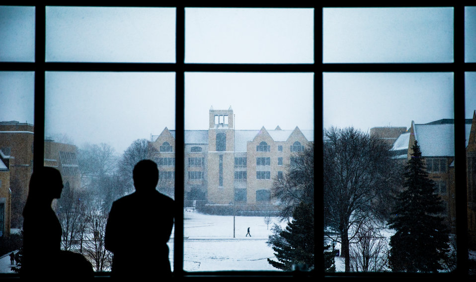 O'Shaughnessy-Frey Library is seen on a snowy day past the silhouettes of people talking inside the Anderson Student Center February 2, 2016.