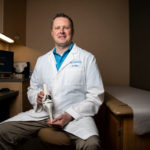 Orthopedic surgeon and University of St. Thomas alumni, Nicholas Weiss ’92, sits for a portrait holding a knee replacement model in the Twin Cities Orthopedics office in Stillwater.