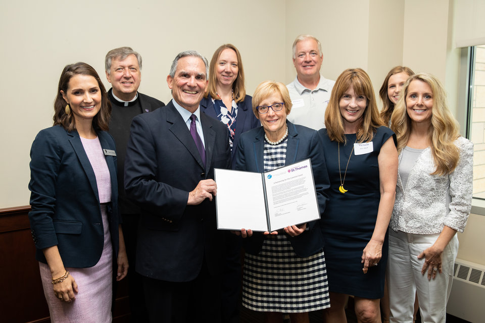 Tim Marx, Catholic Charities president and CEO of Catholic Charities, and President Julie Sullivan hold a document surrounded by staff members.