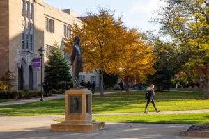 A student walk past the John Ireland statue on a beautiful fall days with bright fall leaves. Mark Brown/University of St. Thomas