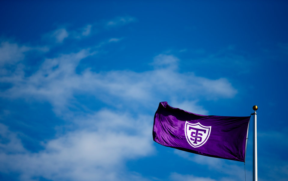 A purple flag with the St. Thomas shield flaps against a blue sky.