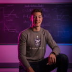 Senior Tommy Anderson, an Actuarial Science major and basketball player, poses for a photo in front of actuarial equations on a blackboard. Mark Brown/University of St. Thomas