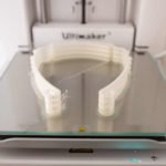 Headbands for medical face shields sit in a 3D printer.