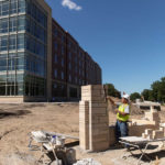 A trades person works on a Kasota Stone base for a new University of St. Thomas sign in front of Tommie North Residence Hall.