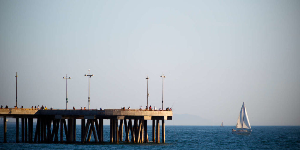 A pier juts into the Pacific Ocean on the coast of Los Angeles, California August 18, 2010. A sailboat plies the waters in the distance.