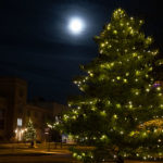 Holiday lights glow on trees below a bright moon on the lower quad.