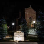 Holiday lights glow on trees in front of the Iversen Center for Faith and Aquinas Chapel.