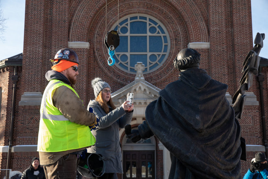 Art History Professor Victoria Young takes photos as a construction crew installs the new sculpture of St. Thomas Aquinas by Canadian artist Timothy P. Schmalz. Mark Brown/University of St. Thomas