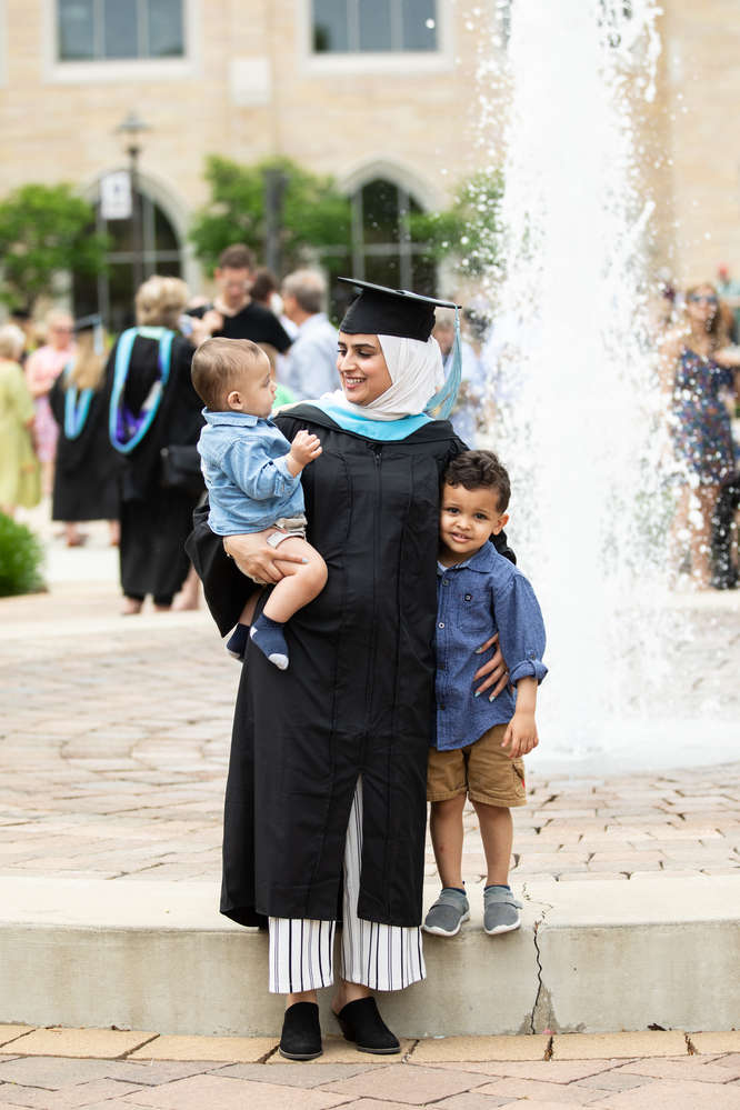 A student poses for a photo with children on Monahan Plaza after the commencement ceremony for graduate programs in the College of Arts and Sciences and the Morrison Family College of Health. Mark Brown/University of St. Thomas