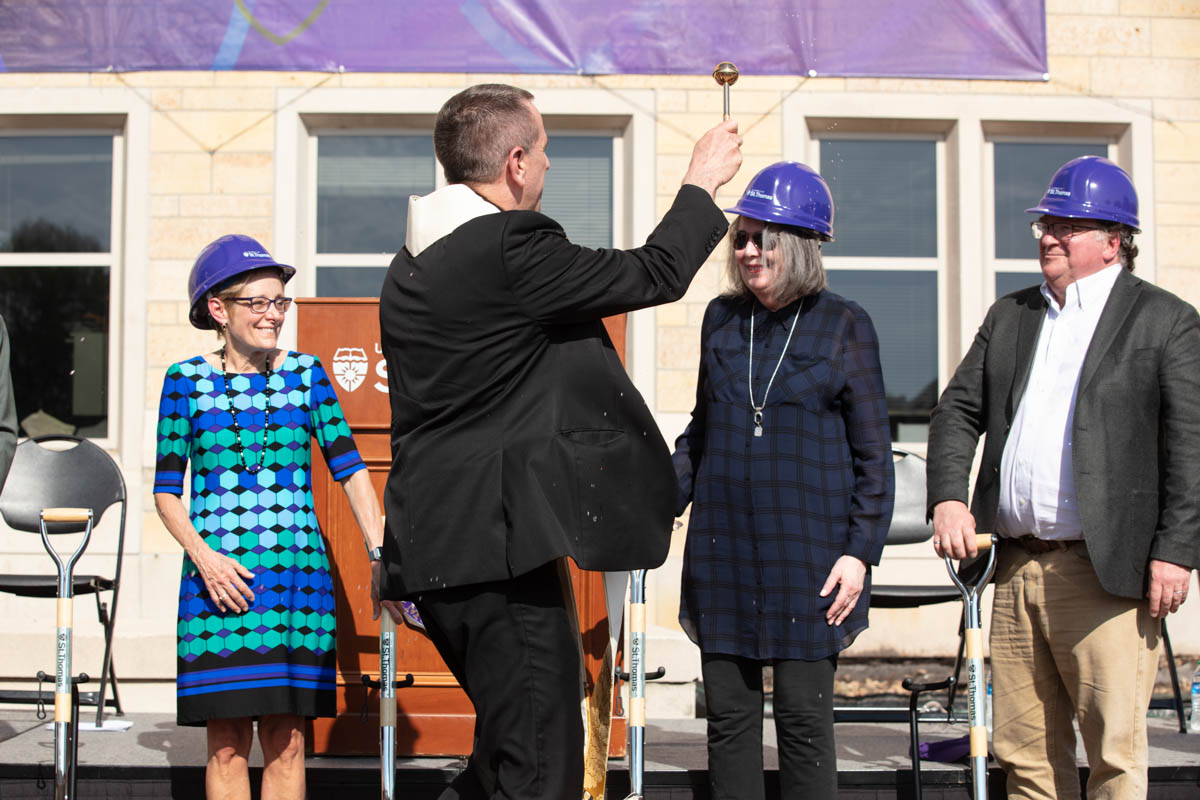 Father Chris Collins makes a blessing with holy water during a groundbreaking ceremony for the Schoenecker Center.