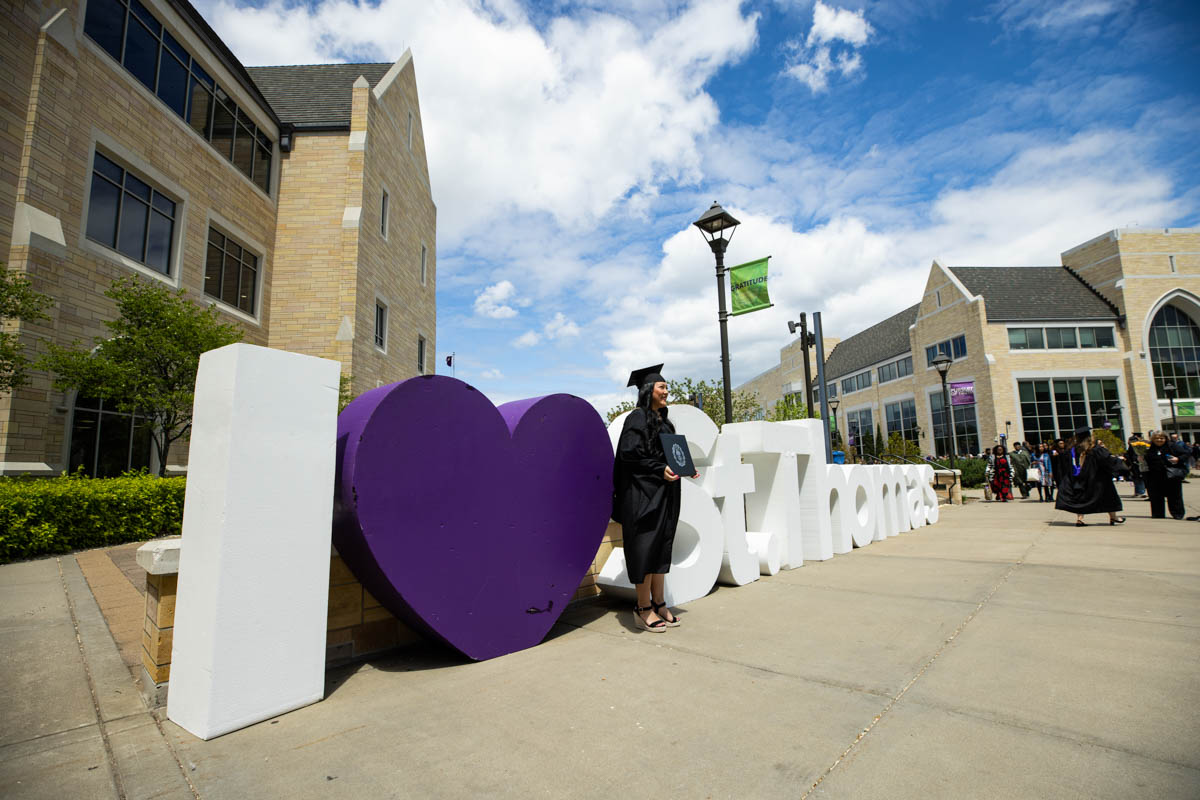A graduate poses for a photo in front of the I Love St. Thomas sign during the 2022 Graduate Commencement ceremony for the Opus College of Business, the School of Education and the School of Divinity in St. Paul on May 22, 2022.