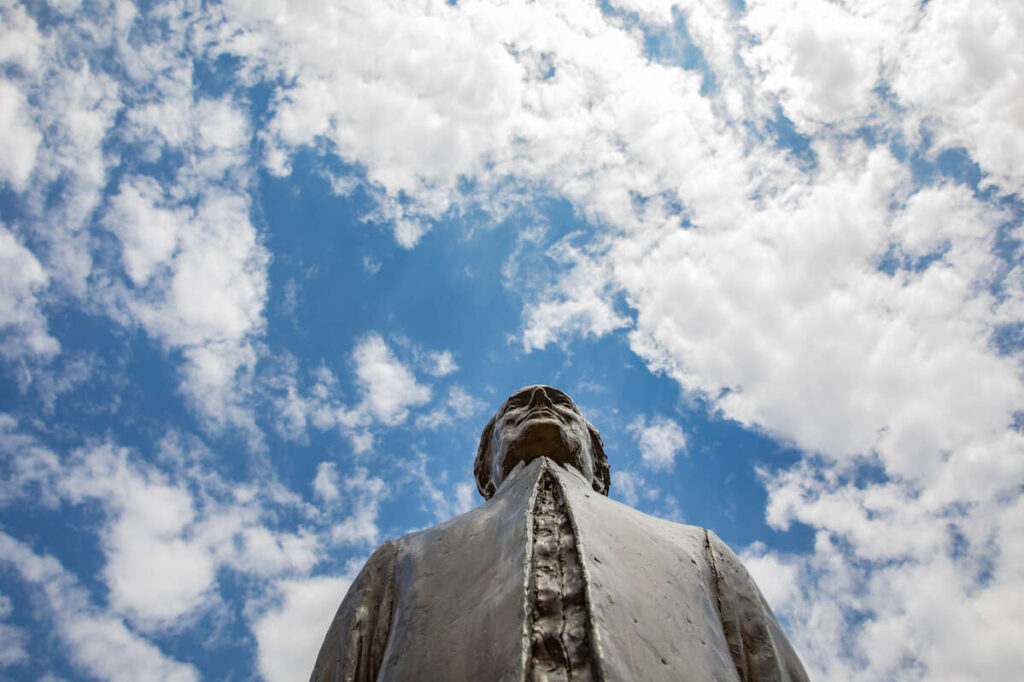 The Statue of Archbishop John Ireland is scene below a blue sky with white clouds on a summer day. Mark Brown/University of St. Thomas