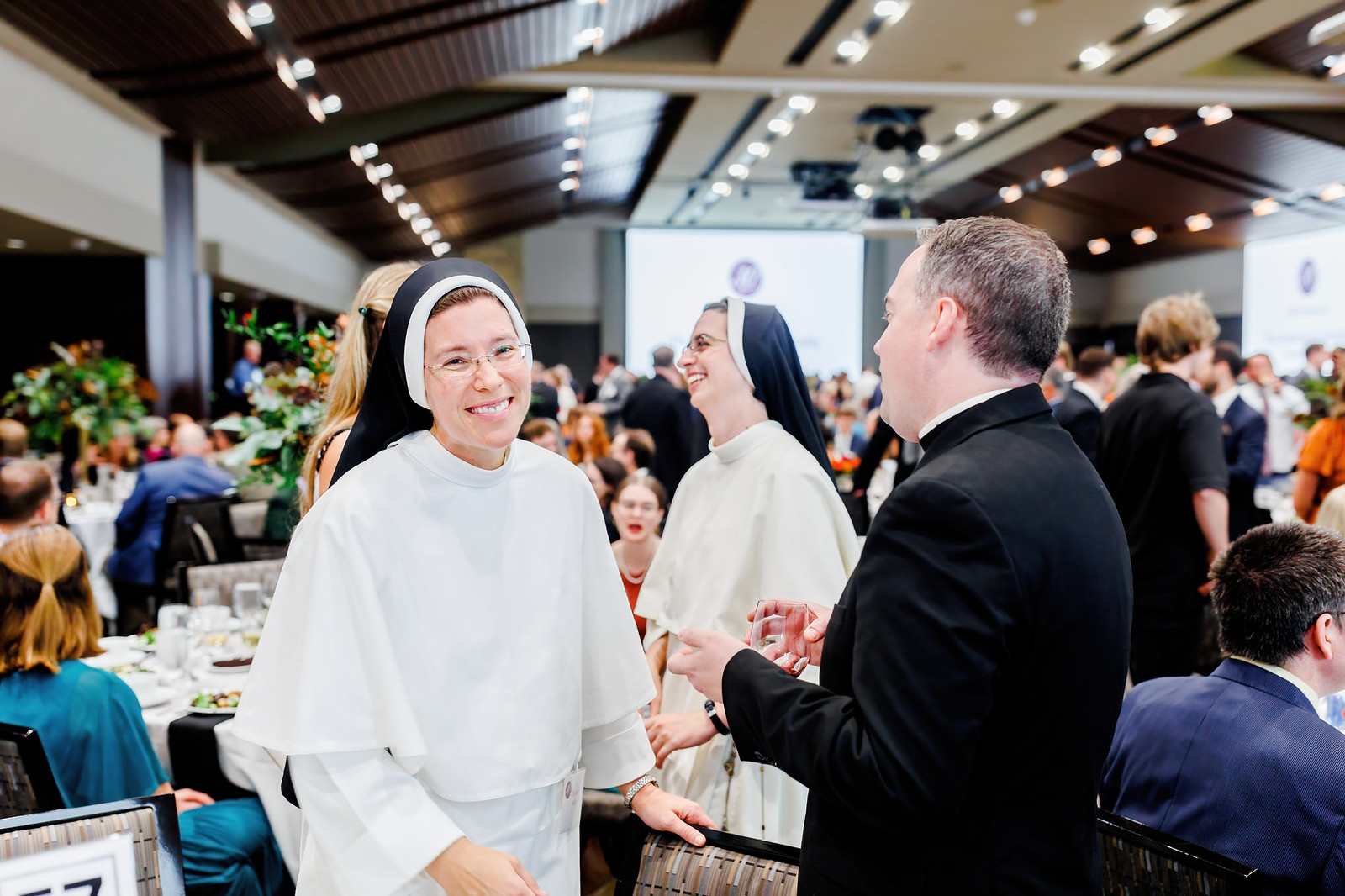 A nun smiling kindly surrounded by many people at a decorated banquet.