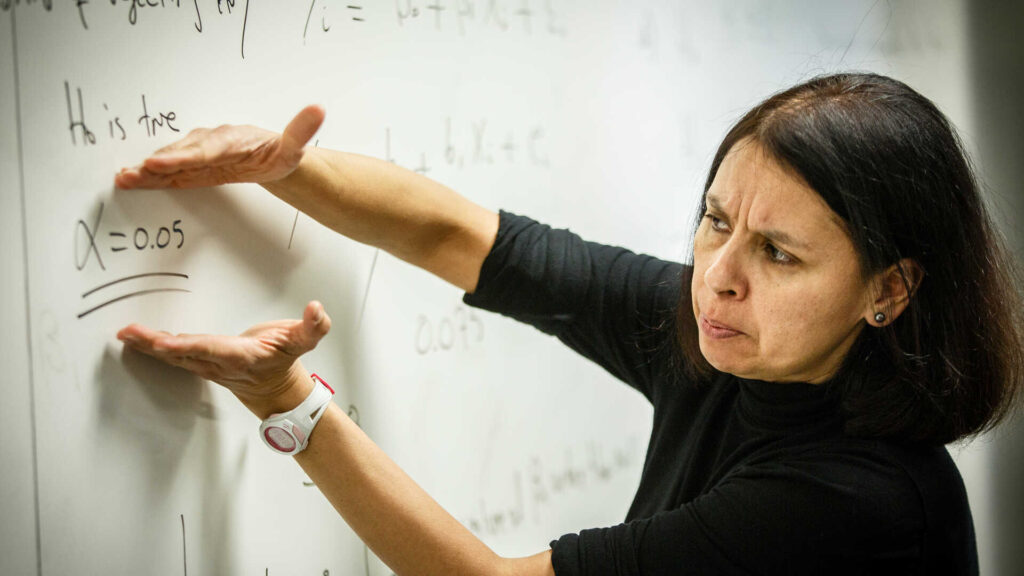 Economics Professor Luz Saavedra points to a whiteboard while teaching an Economics Forecasting class.
