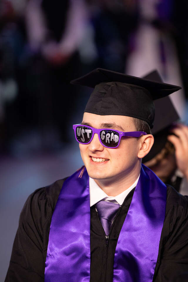 A student wearing UST GRAD sunglasses during the 2024 Opus College of Business Undergraduate Commencement Ceremony.