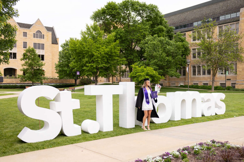 A student poses for photos with the St. Thomas sign after the 2024 Morrison Family College of Health, School of Education and School of Engineering Undergraduate Commencement Ceremony on the quad in St. Paul on May 25