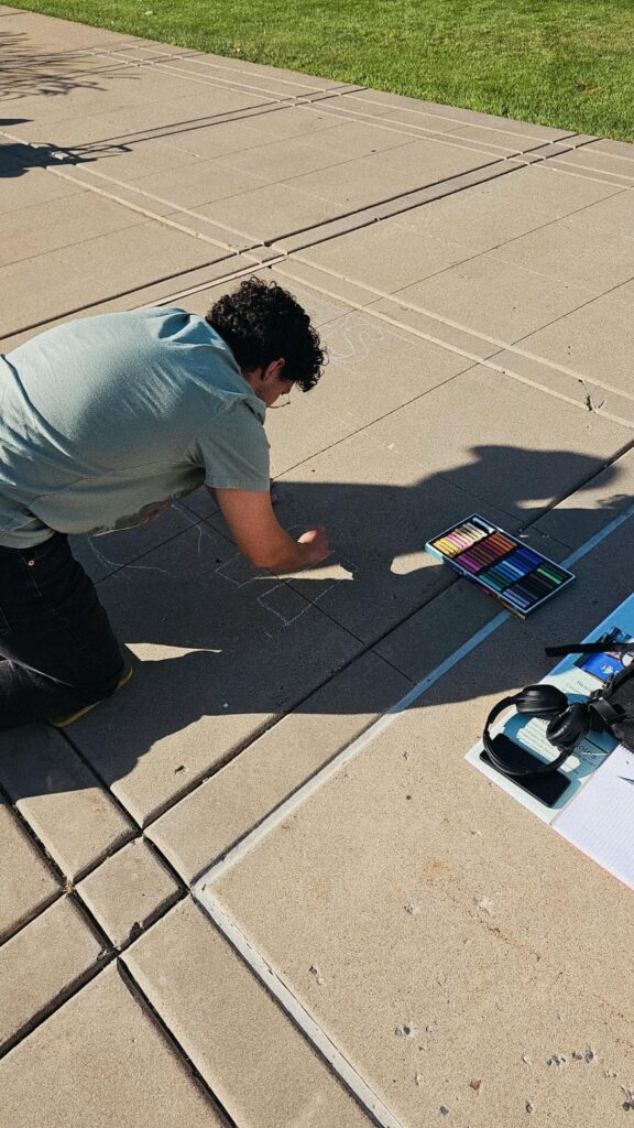 Student Hapaki Lorenzo kneels on the ground drawing with chalk. 