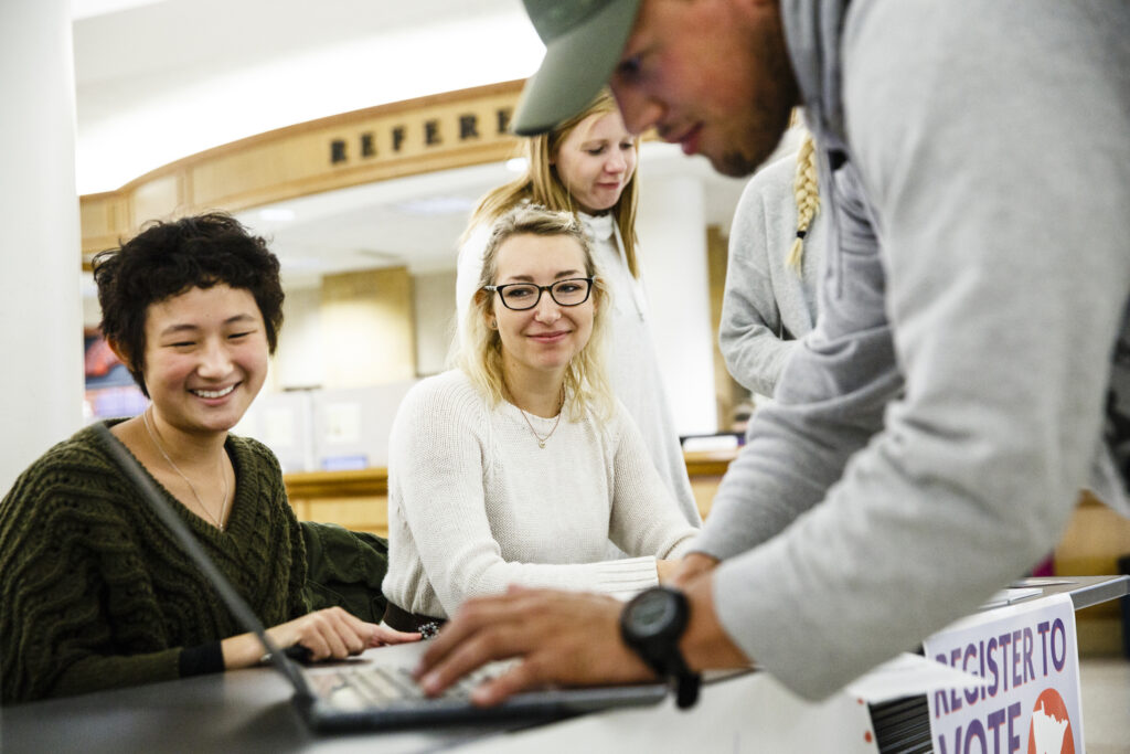 Students smile during a voter registration drive by School of Social Work and Justice and Peace Studies students on October 13, 2016 in  the O'Shaughnessy-Frey Library Center. Registering to vote (wearing a baseball hat) is student Josh Herman. Left is Devine Zheng (Justice and Peace Studies), right is Hannah Ruskin (School of Social Work).