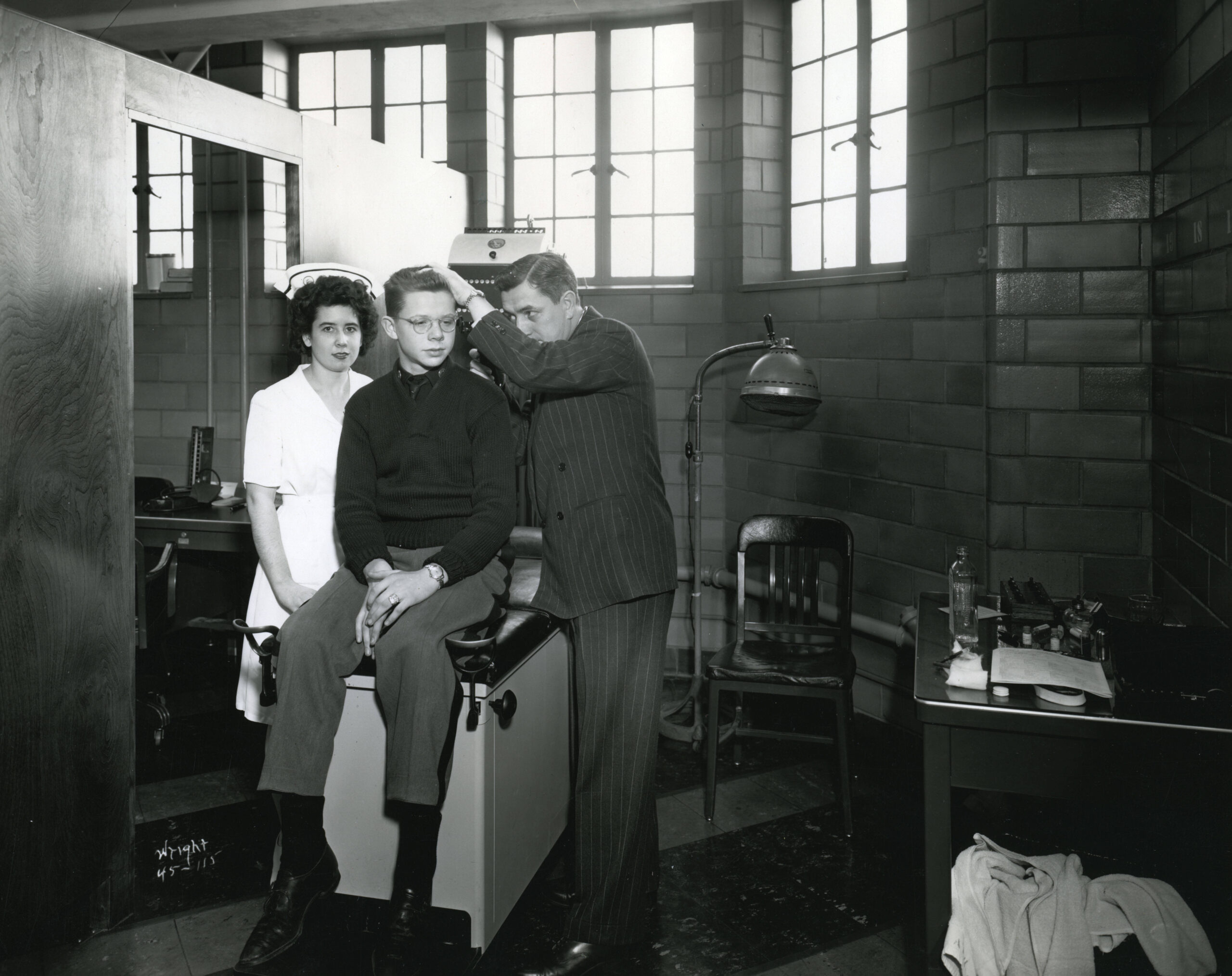 A nurse on the left stands by as a man examines a boys head as the boy sits on a table.