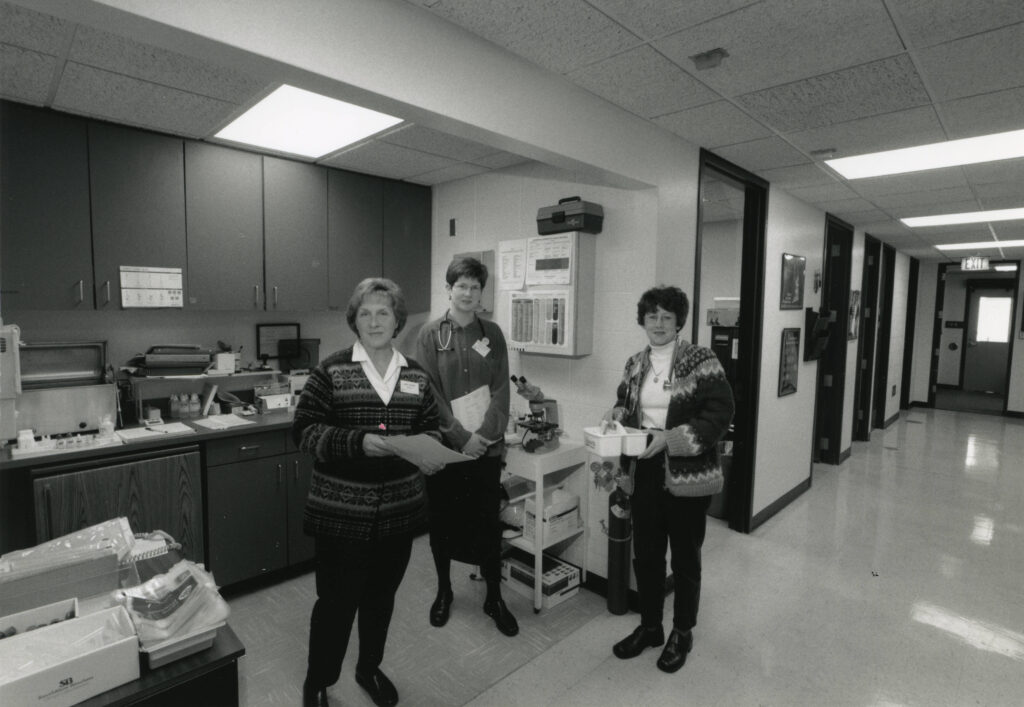 Three women stand in the middle of a clinic room.