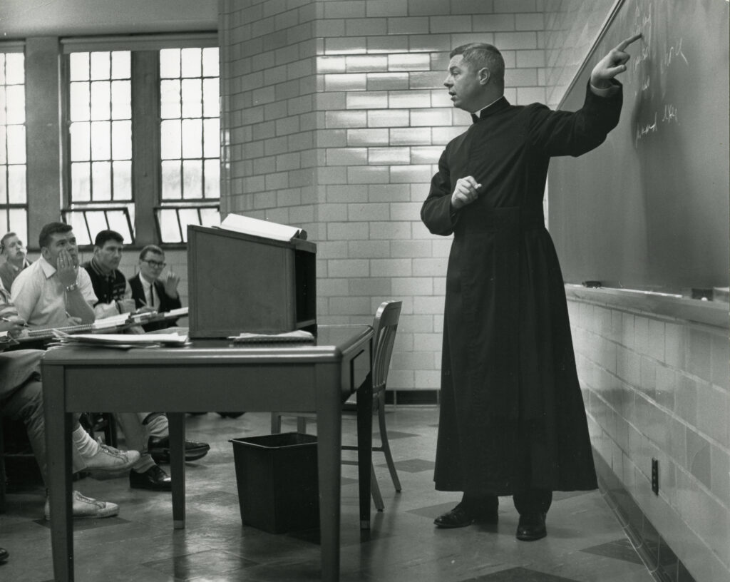 Man pointing at a chalkboard. Black and white. 