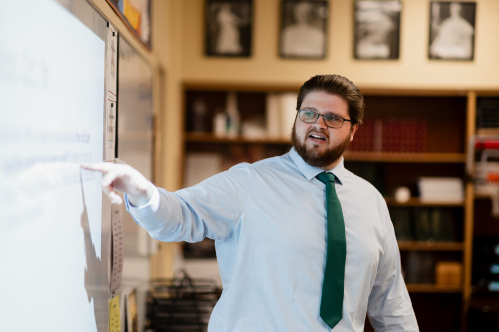 Man pointing to the board in a classroom. 