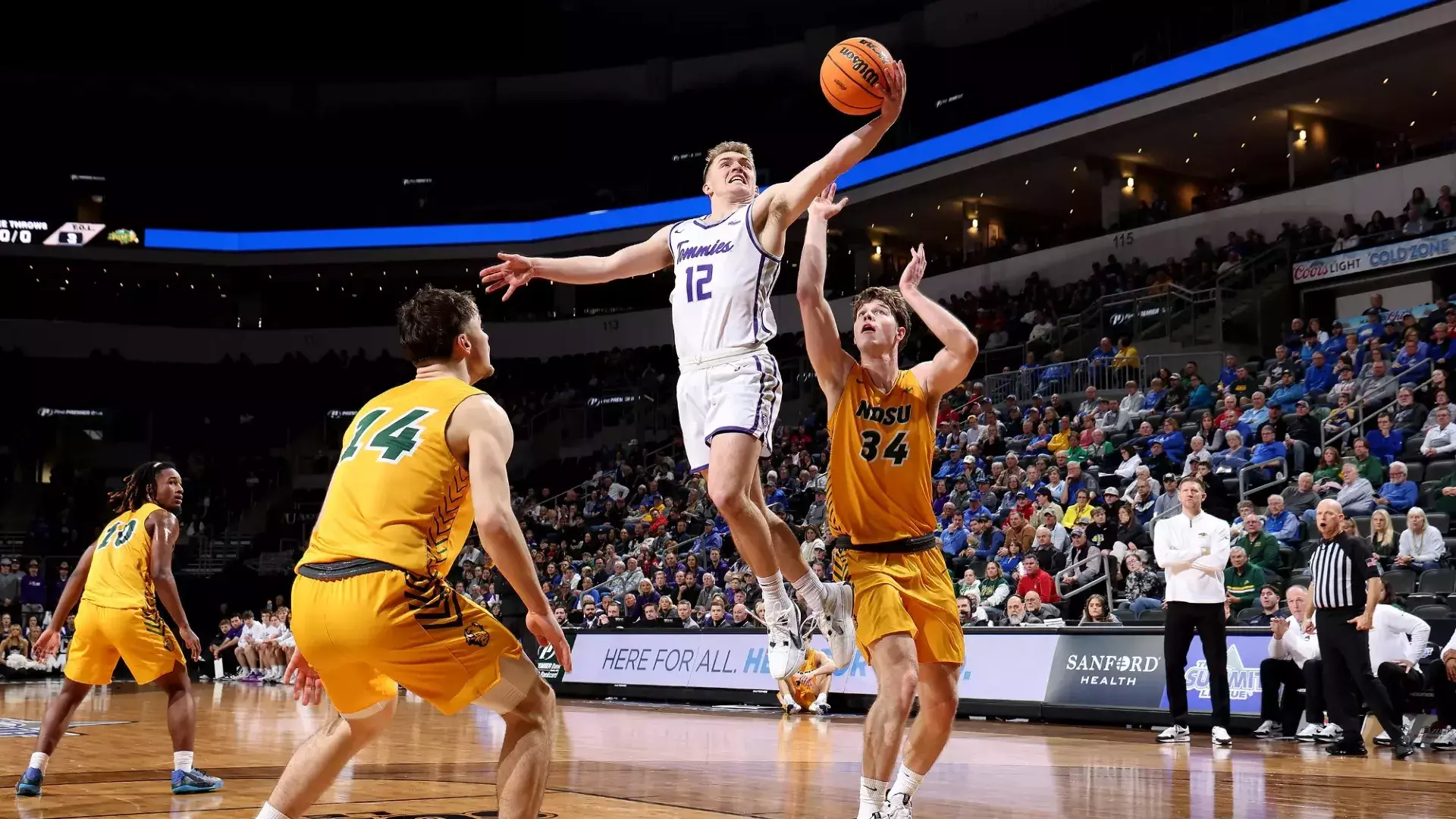 St. Thomas Basketball game. Student is seen mid-air shooting a basketball, with two students on the opposing team attempting to block him.