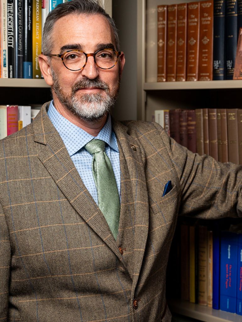 Dr. Mark DelCogliano stands in front of a bookshelf.