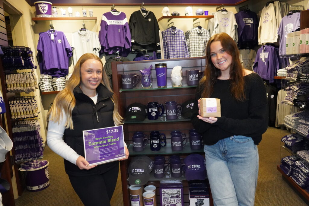 Clara Mattson holds up a Tommie Blend sign and Brenna Keil holds the Tommie Blend inside the Tommie Shop.