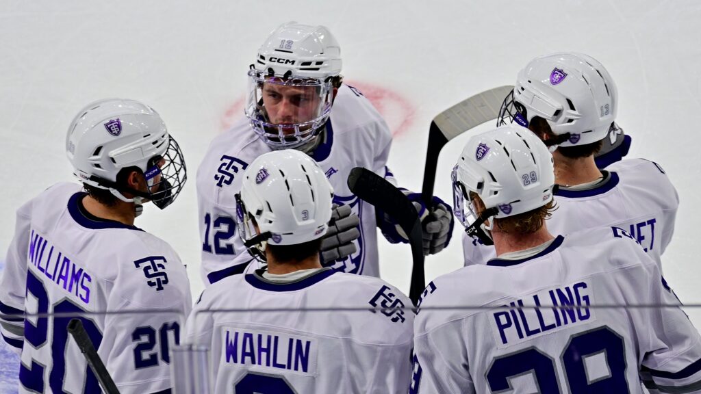 Five St. Thomas men's hockey athletes huddle on ice.