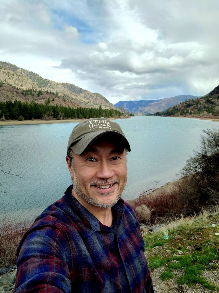 A man stands with a lake and forest behind him.