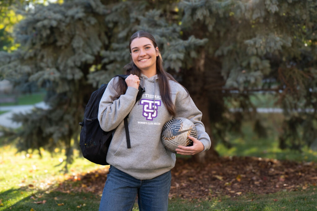 Norah Barry carrying a backpack and holding a soccer ball.