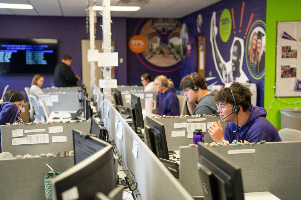 Students sitting in cubicles with telecommunications headsets.