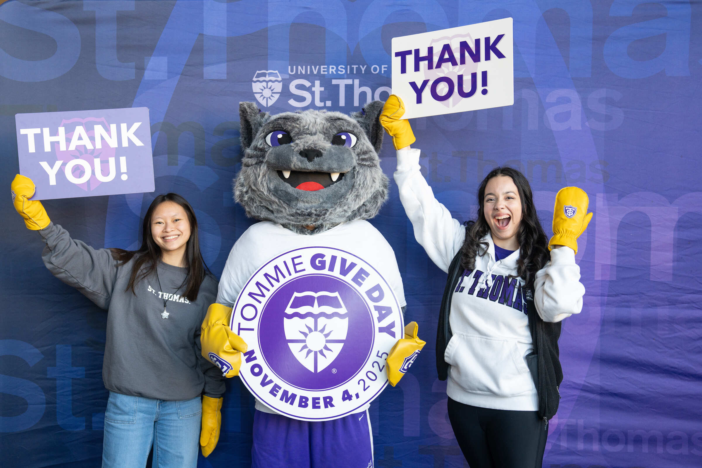 The Tommie mascot in between two students holding up thank you signs
