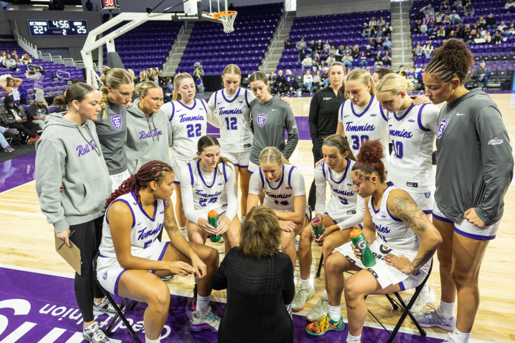 St. Thomas women's basketball team huddles around the coach.